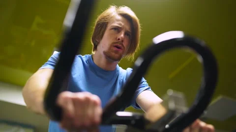 Red-haired guy in a blue t-shirt rides a bicycle in the gym. close-up of a hand Stock-Footage 163459212
