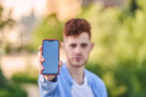Red-haired hispanic young man showing a screen smartphone in the city. Foto stock