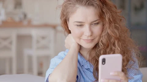 Red haired lady using mobile phone at home Stock Footage 200995740