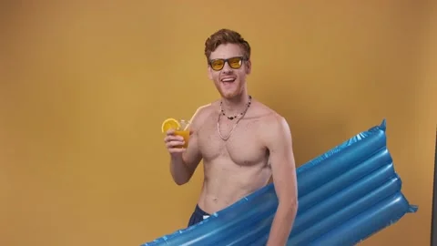 Red-haired man in beach shorts with an inflatable mattress and a cocktail points Stock Footage 241913003