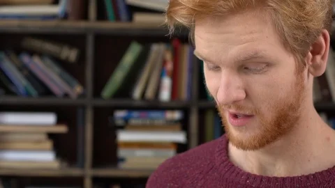 Red-haired man in library reading story joyful Stock Footage 121538895