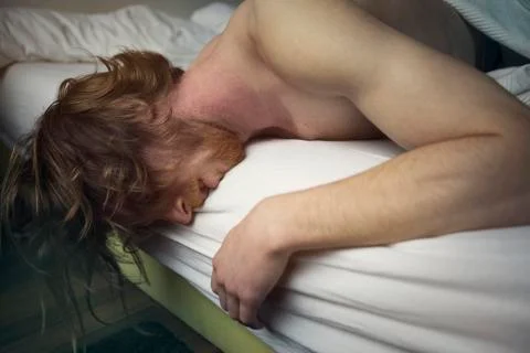 Red-haired man lying in bed looking sick Stock Photos