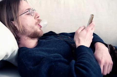 Red-haired man lying on couch texting on phone Stock Photos