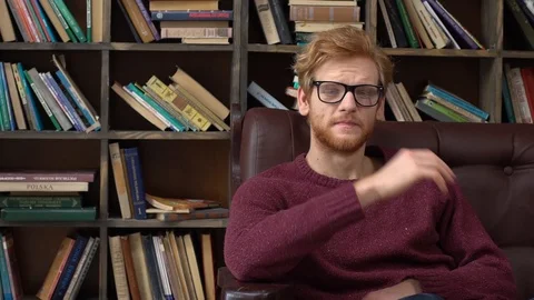 Red-haired man sitting in library massaging nasal bridge Stock Footage 121646227