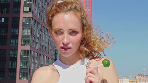Red-Haired model holds green round lollipop on rooftop, enjoying view over city Stock Footage 160559400