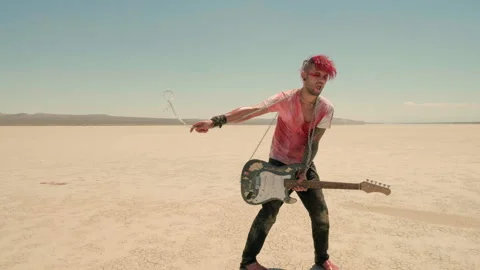A red-haired punk wraps a chain around his neck, screaming in rage in the desert Stock Footage 293118447