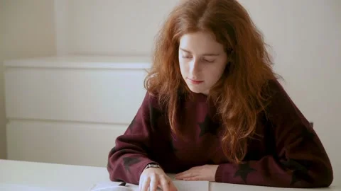 A red-haired schoolgirl does her homework and reads carefully Stock Footage 160170673