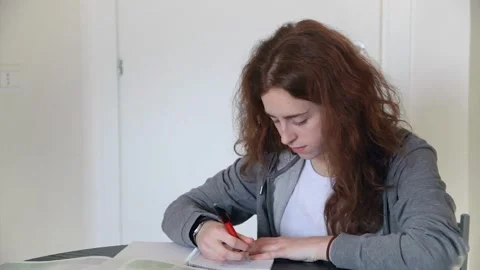A red-haired schoolgirl is doing homework, suddenly raises her head and smiles Stock Footage 160188562