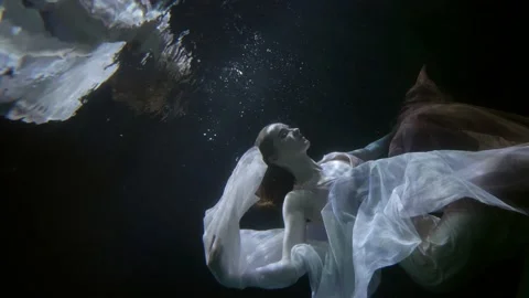 A red-haired woman hovers with a translucent cloth in dark water and is Video stock 208378352