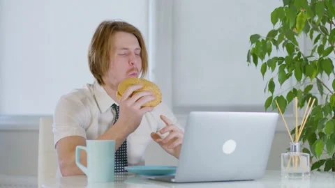 Red-haired young male worker in the office.eating a burger in tasty laptop 動画素材 239271744