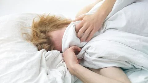 Red-haired young man lying in bed covering up his face Stock Photos