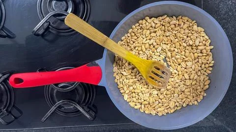 Red-handled frying pan with roasted peanuts and a wooden spoon Stock Photos