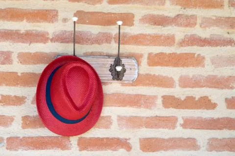Red hat hanging on a coat hook against a brick wall background Stock Photos