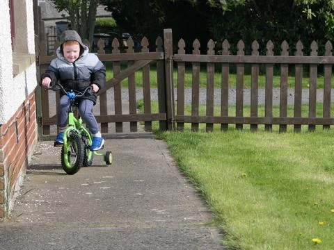 Red headed boy having fun playing on his bike in a garden Stock Photos