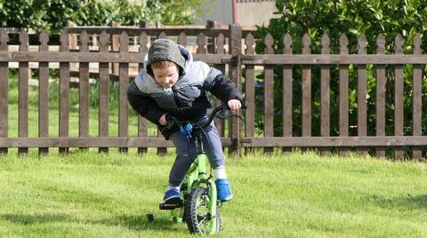 Red headed boy having fun playing on his bike in a garden Stock Photos