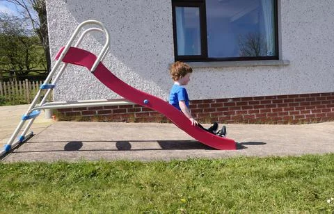 Red headed boy playing on a red slide in a garden Stock Photos