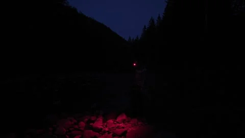 Red Headlamp Beam Sweeping Across Rocky Riverbank Ground at Night Stock Footage 344894375