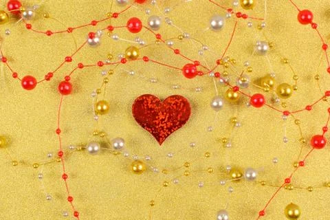 Red heart with beads on a gold background. Stock Photos
