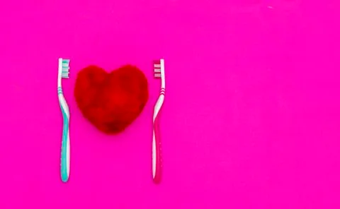 Red heart between two toothbrushes on pastel pink background. Male and female 库存照片