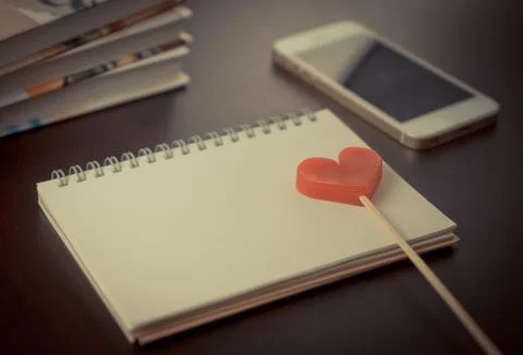 Red heart on blank notebook on working desk with phone Stock Photos