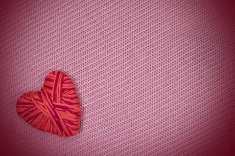 Red heart made of thread on a pink knitted pattern background texture. 写真素材