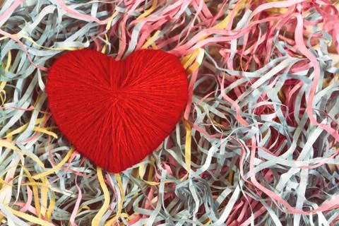 A red heart made of woolen threads lies on a colored serpentine. Stock Photos
