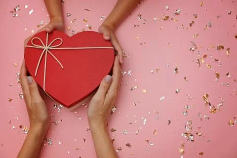 Red heart shape gift box on festive pink background, with child's and mom's Stock Photos