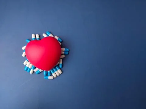Red heart shape surrounded by blue and white medical capsules on a blue bac.. Stock Photos