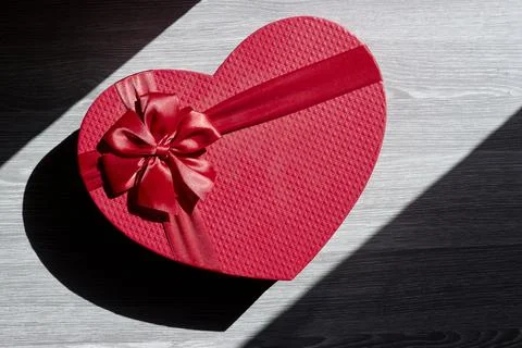 Red heart-shaped gift box with a satin ribbon bow sits on a dark wood surface Stock Photos