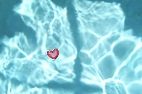 Red heart-shaped object floating in clear blue water. 스톡 사진