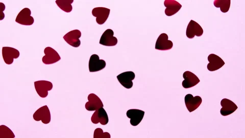 Red heart-shaped sequins are spinning in a circle on a pink background Stock Footage 168933747