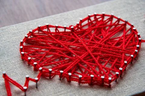 Red heart string art made with tangled yarn on metal nails on canvas background Stock-Fotos