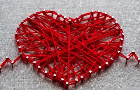 Red heart string art made with tangled yarn on metal nails on canvas background Stock Photos