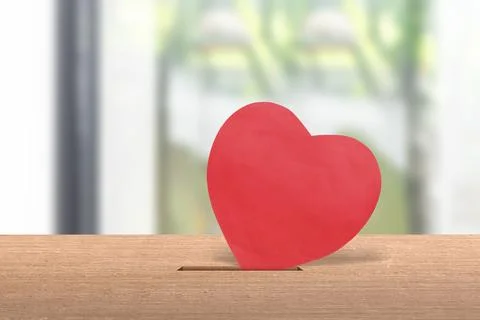 A red heart symbol being inserted into a slot on a wooden surface, represen.. Foto stock