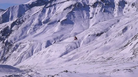 Red helicopter flies over high mountains covered with snow Stock Footage 116600423