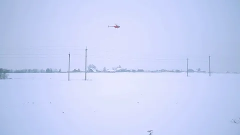 A red helicopter is flying over the field and power lines. Shooting from the Stock Footage 80319133