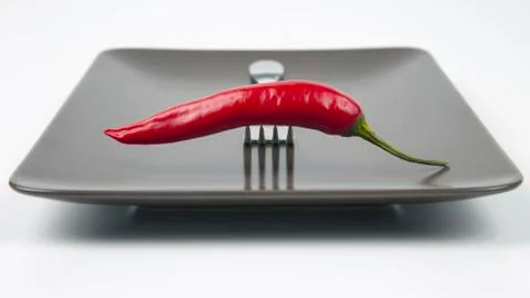Red hot pepper with fork close-up on grey plate. Healthy vegetable food and v Stock Photos