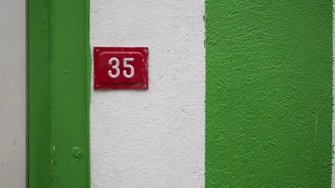 Red house number thirty five on white and green wall section showing urban .. Vídeos de archivo 332116462