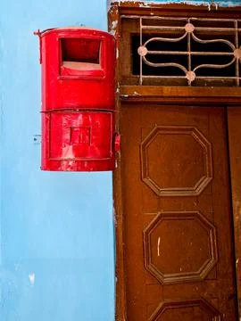 Red Indian post box mounted on a blue wall in a small village town showing the Stock Photos