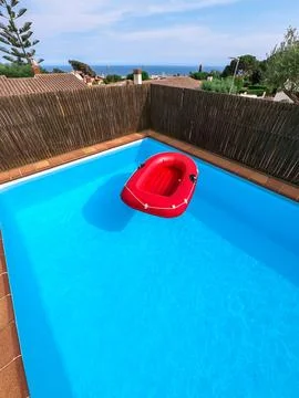 Red inflatable boat floating in a private swimming pool, no people. Stock Photos