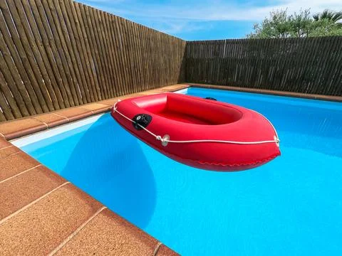 Red inflatable boat floating in a private swimming pool, no people. Stock Photos