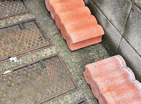 Red interlocking bricks stacked near a concrete wall beside metal access cove Stock Photos