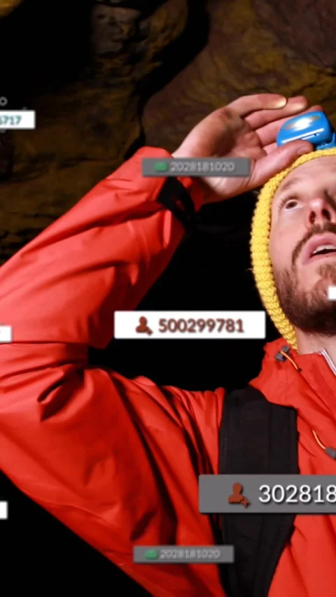 Red-jacketed explorer raising blue headlamp mapping cave as tech overlays 스톡 동영상 331030150