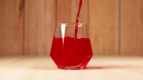 Red juice pouring into a diamond shaped glass on wooden background in slow .. Stock Footage 333492505