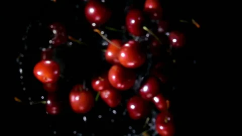 Red juicy cherries bounce up with splashes of water on a black background Stock Footage 125755446