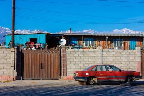 Red junked car without wheels in front of brick fence of junkyard, outside Stock Photos