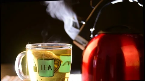 Red kettle in the background with cup of tea dropping the front both giving o Video stock 154704839