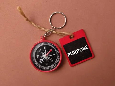 A red keychain compass attached with a string to a red tag labeled PURPOSE .. Stock Photos