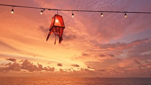 Red lantern beach light with lightbulbs are hanging on wired line above beach Stock Footage 128593299