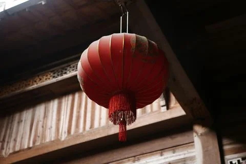 A red lantern hangs from the eaves of an ancient wooden house, adorned with.. Stock Photos